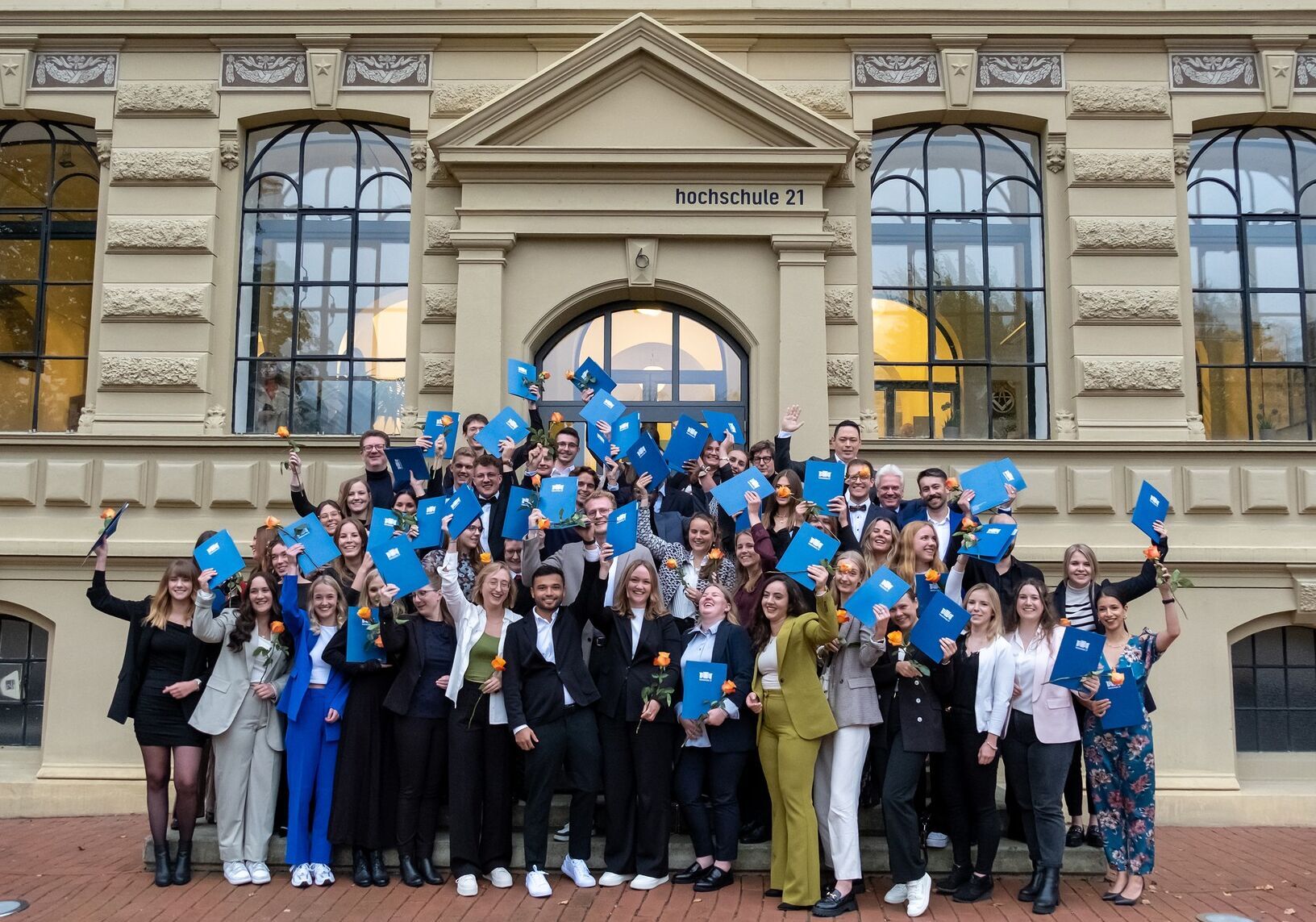 Gruppenfoto der jubelnden Absolventinnen und Absolventen auf der Treppe vor dem Gebäude der hochschule 21