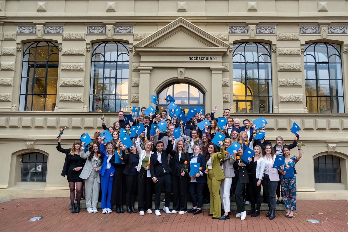 Gruppenfoto der jubelnden Absolventinnen und Absolventen auf der Treppe vor dem Gebäude der hochschule 21